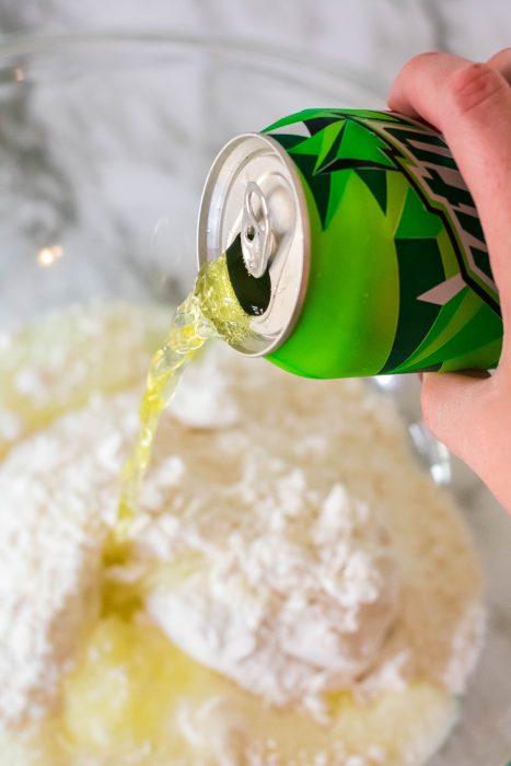 Mountain dew being poured over a cake mix for a 2 ingredient mountain dew cake. 