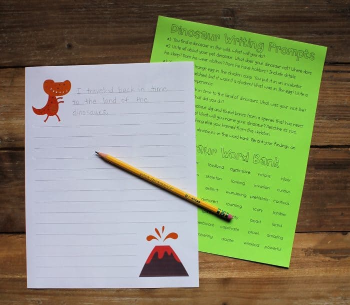 Printable dinosaur writing prompts printed on white and green paper, with a pencil laid across them.