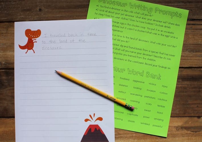 Printable dinosaur writing prompts printed on white and green paper, with a pencil laid across them.