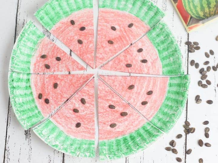 A paper plate colored to look like a watermelon with a green rim and red inside, with watermelon seeds on the plate.