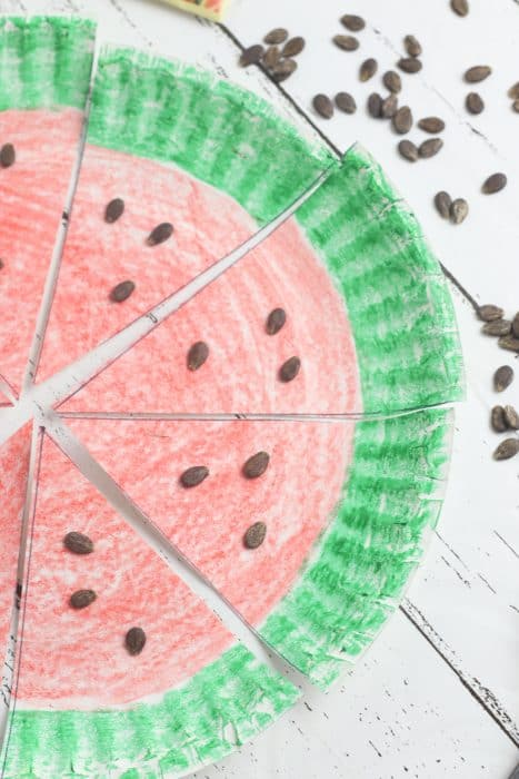 A paper plate colored to look like a watermelon with a green rim and red inside, with watermelon seeds on the plate. 