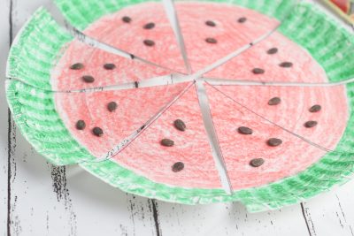 A paper plate colored to look like a watermelon with a green rim and red inside, with watermelon seeds on the plate.