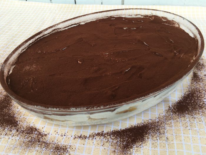Traditional tiramisu in a glass bowl, featuring chocolate powder sprinkled on top.