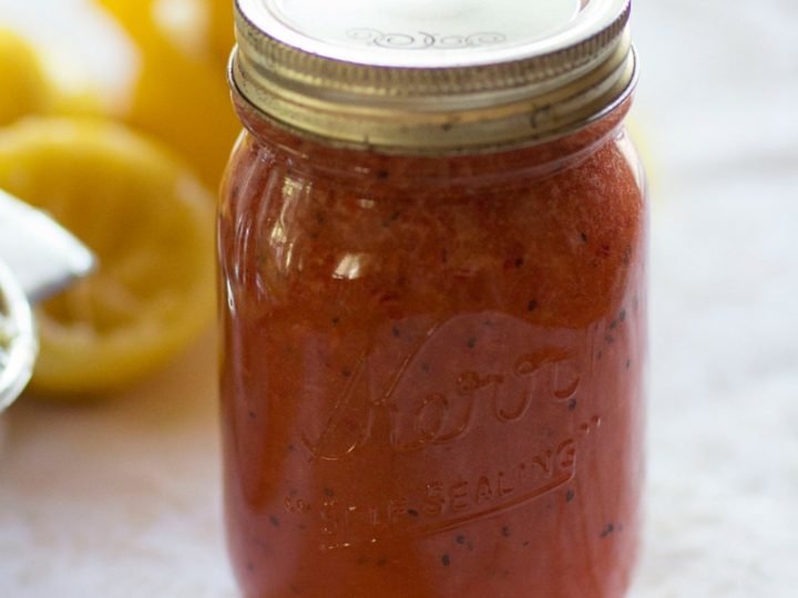 Cranberry Lemon Jam in a jar with lemons behind it.